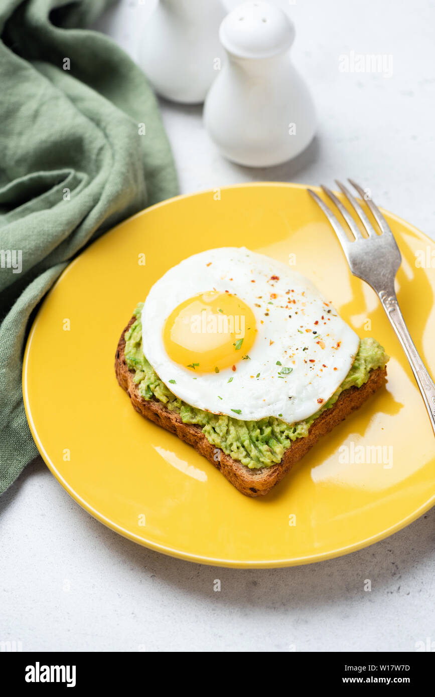 Toast with fried egg and avocado on yellow plate. Tasty breakfast, lunch or snack Stock Photo