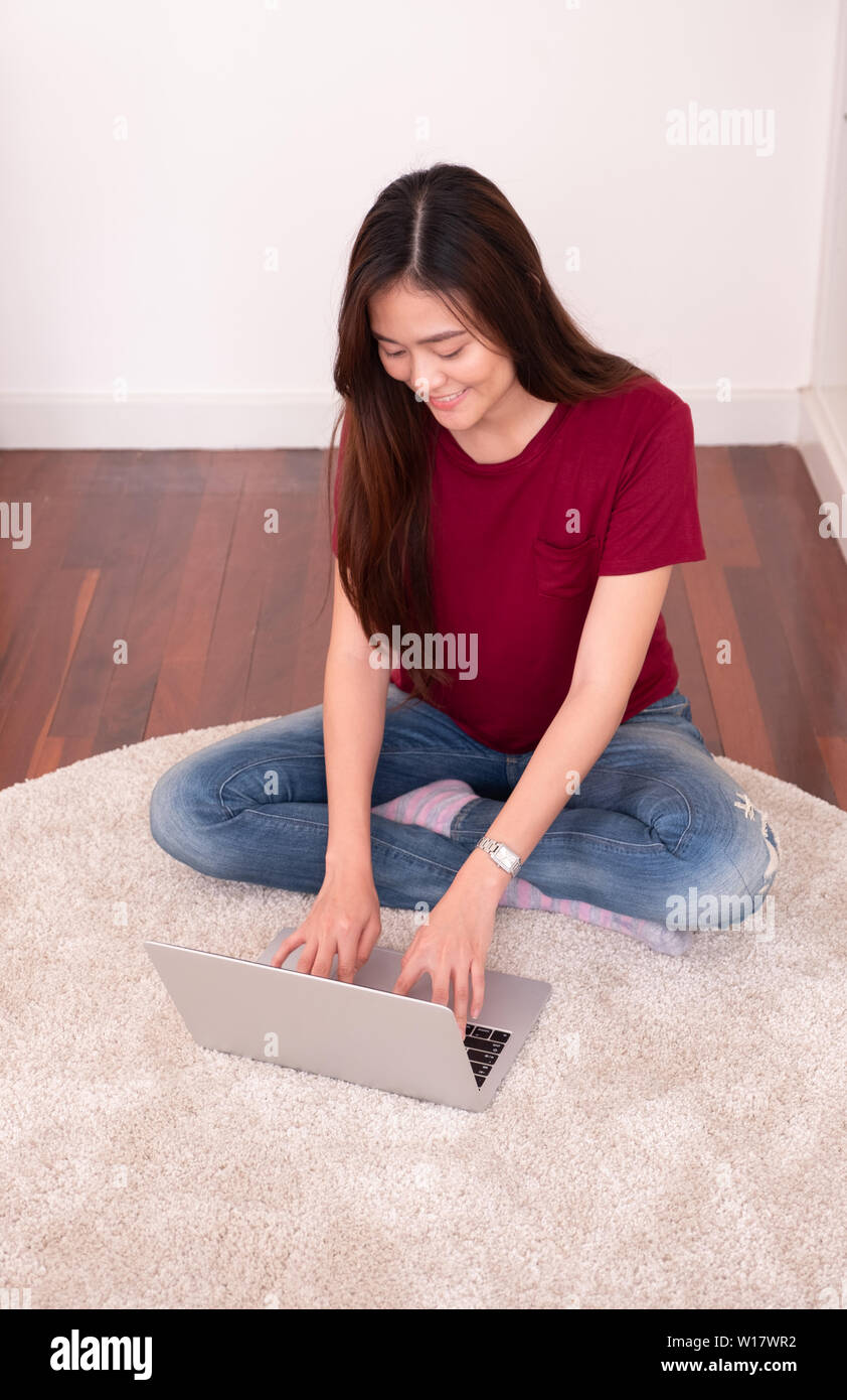 Happy asian woman working on laptop computer at home.female freelancer sitting on carpet on floor work at home in living room. Stock Photo