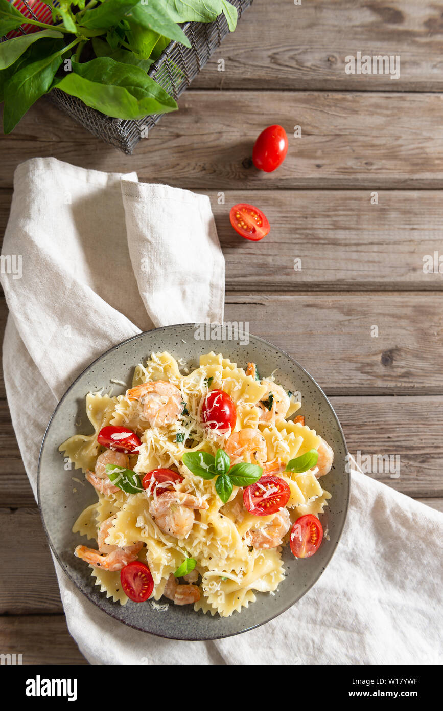 Italian pasta farfalle in a creamy garlic sauce with shrimps, cherry tomatoes and basil on a plate, top view. Copy space Stock Photo