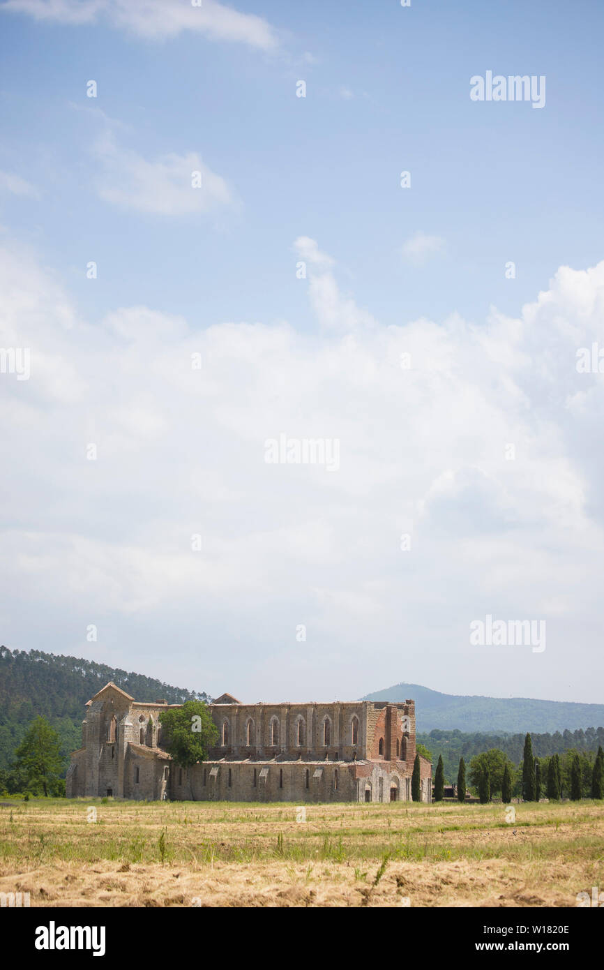 Distant landscape view of san galgano abbey under a moody summer  sky with cypresses on its side. Chiusdino, Tuscany, Italy. Vertical shot. Stock Photo