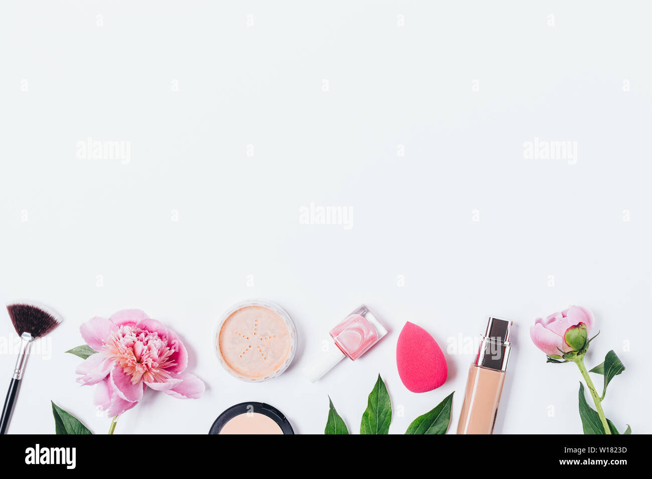 Top view row of makeup products, face powder, foundation, sponge beauty blender, cosmetic brushes and fresh pink peony flowers on white background wit Stock Photo