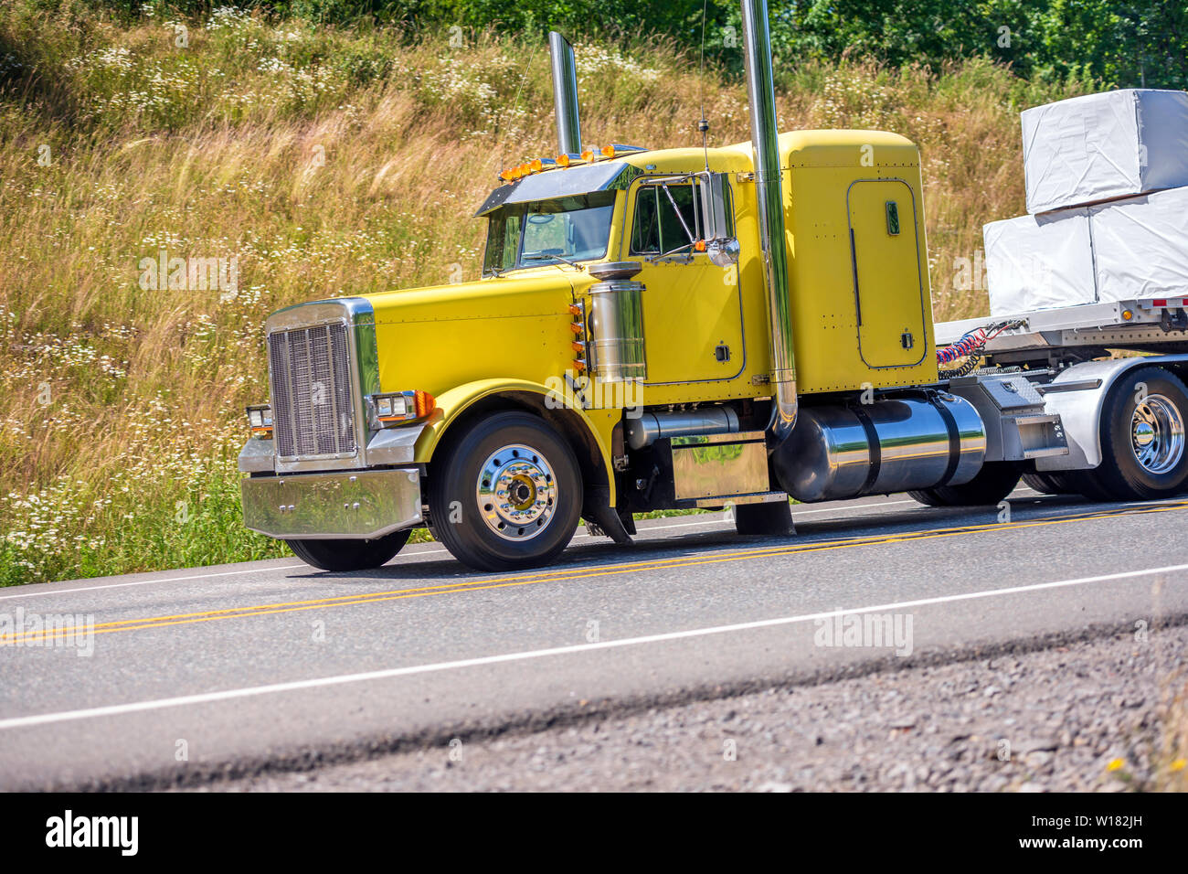 Big rig yellow classic long haul semi truck with flat bed semi trailer
