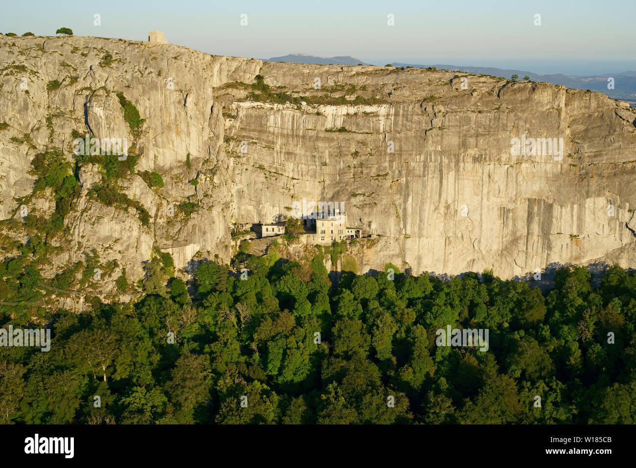 AERIAL VIEW. Sanctuary of Sainte-Baume on the ledge of a rock face and a chapel standing on the clifftop. Plan d'Aups, Provence, France. Stock Photo