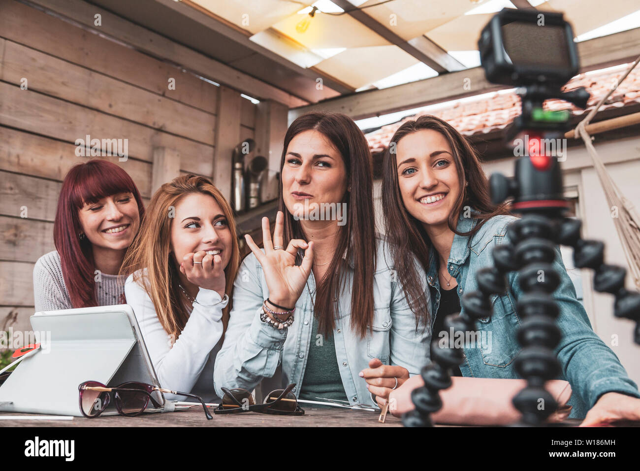 four young  vloggers talking on the camera leaning against a small tripod outdoors Stock Photo