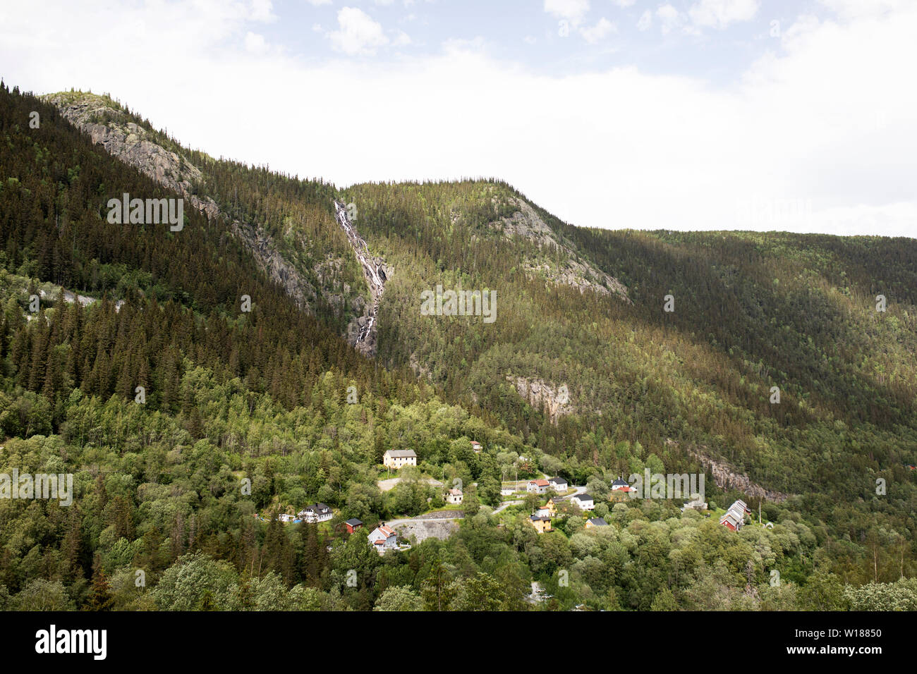 A valley with houses lies under the Våeråifossen waterfall near Vemork, Rjukan, Norway. Stock Photo