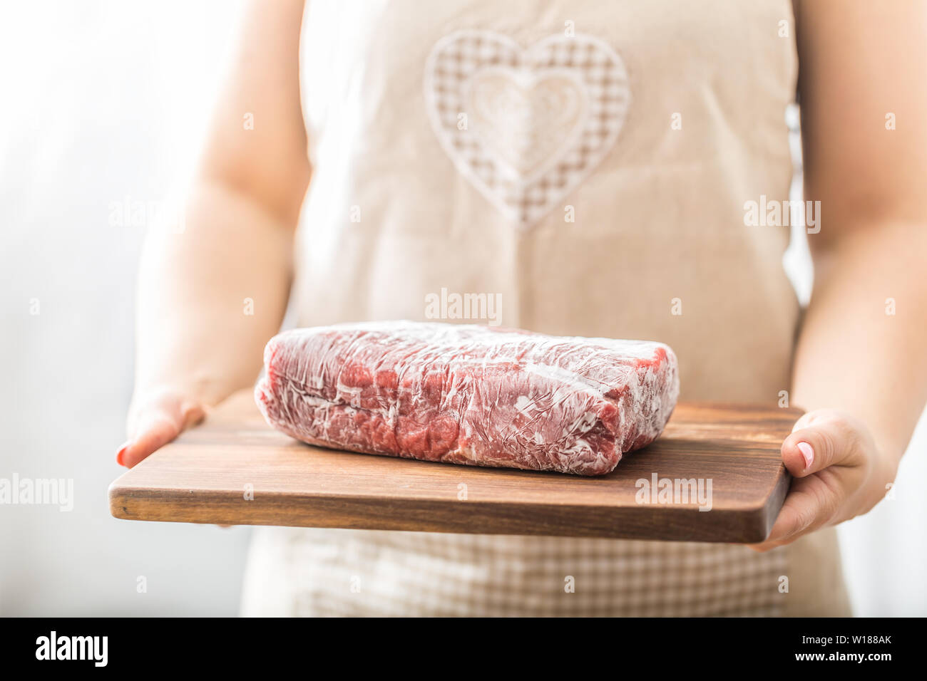 Female cook holding wooden board of raw and frozen beef  meat Stock Photo
