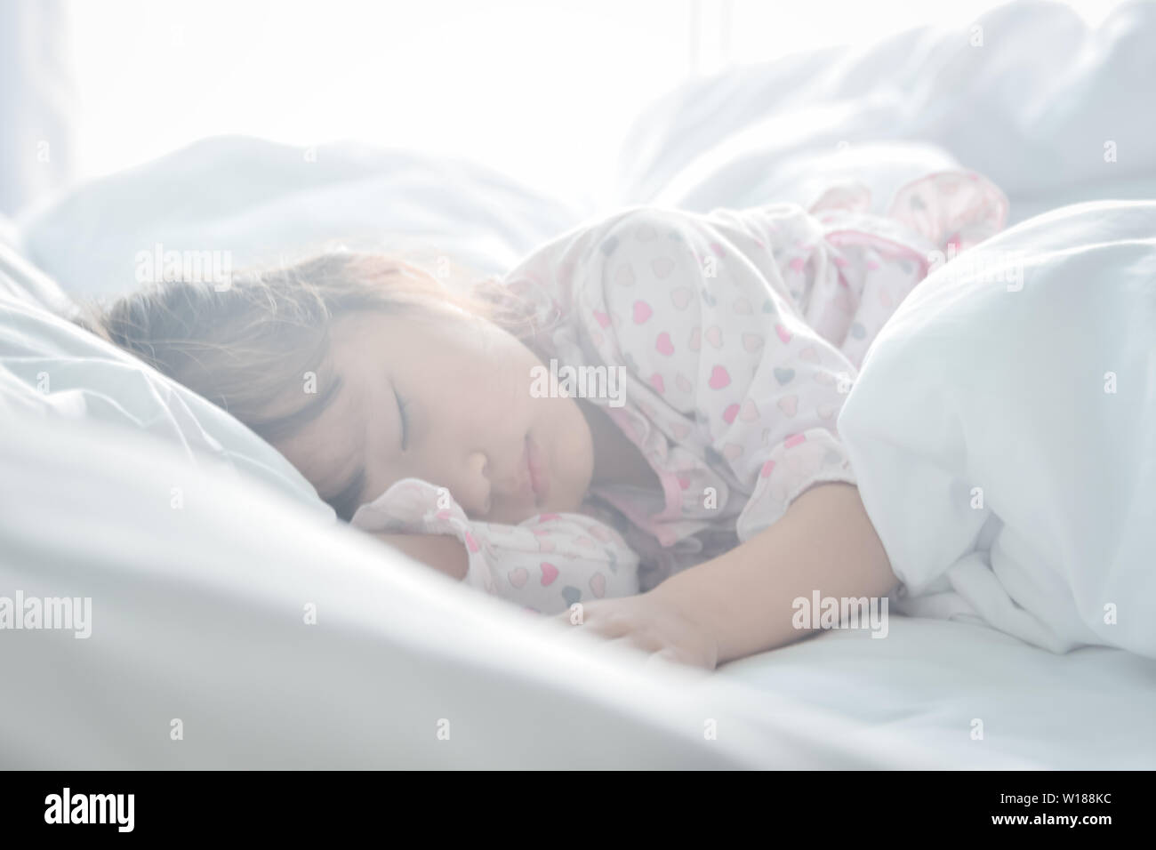 Asian little girl sleeping in the bed on the morning time with sunrise light soft focus sweet dream concept Stock Photo