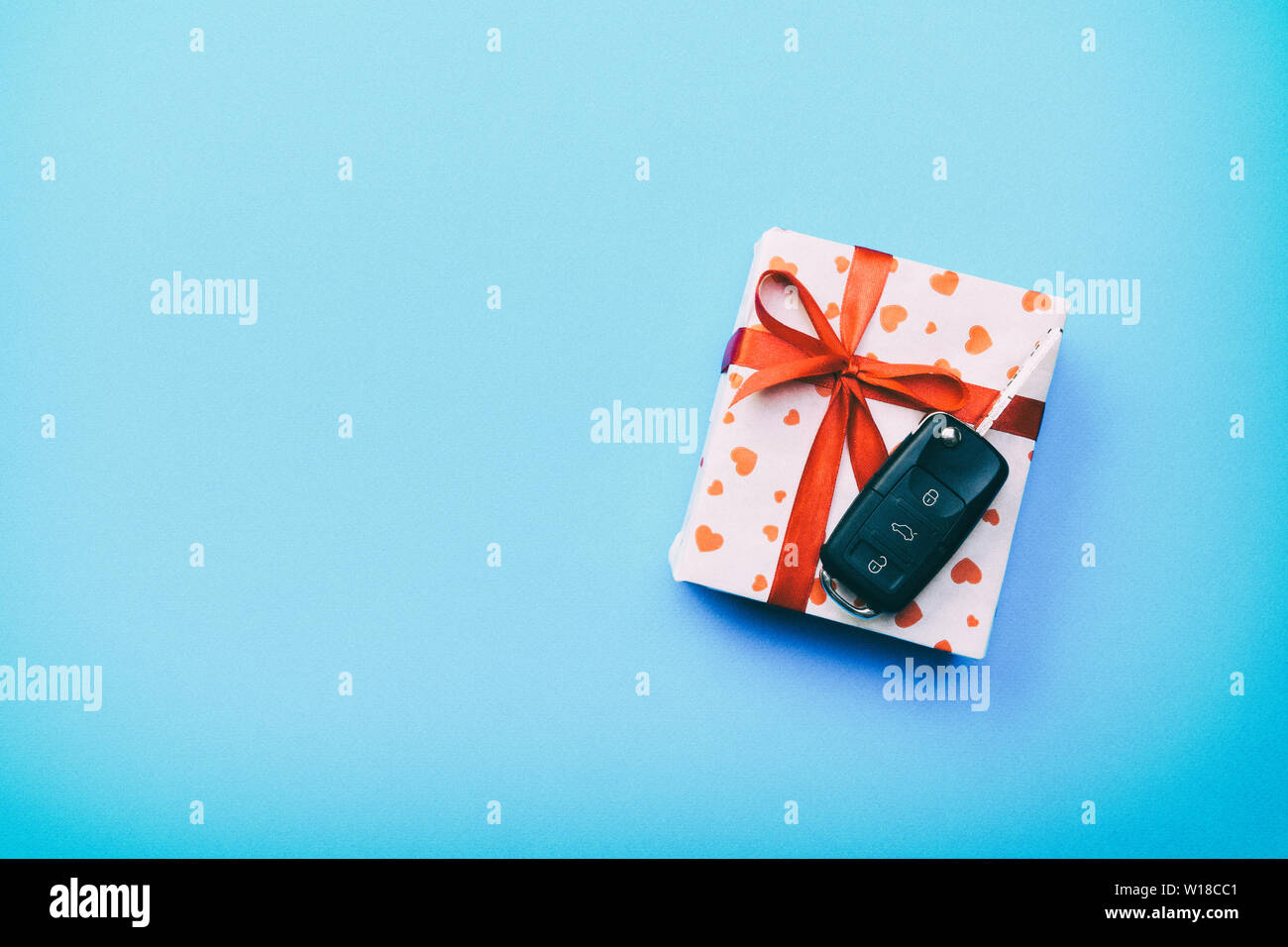 Car key on paper gift box with red ribbon bow and heart on blue table ...
