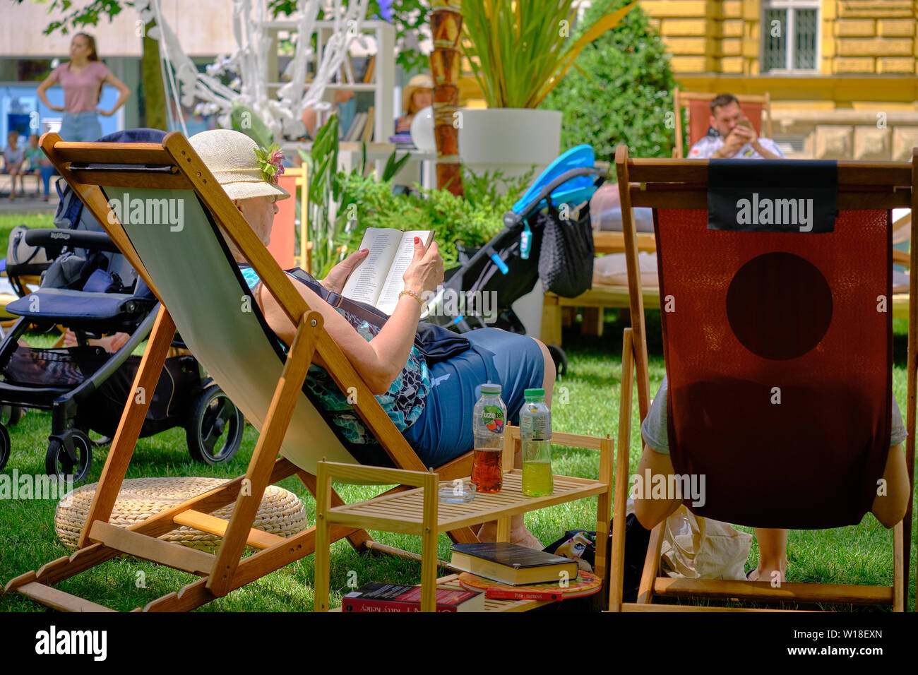 Zagreb, Croatia, July 1, 2019.  Lumen Station installation in Park. View from behind of Woman siting in sponsored deck chair  in shade from umbrellas Stock Photo