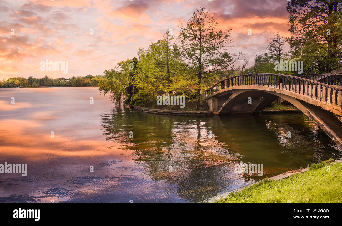 Footbridge over the pond in the city park at sunset. Styled stock photo with wooden bridge in twilight atmosphere in Herastrau Park from Bucharest. Ro Stock Photo