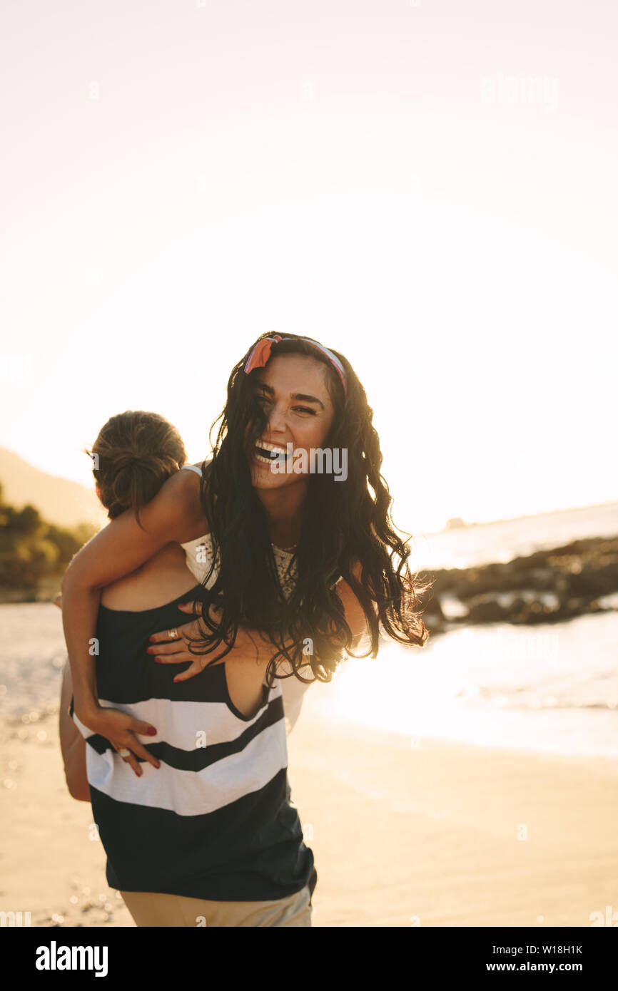 Man walking on beach carrying his girlfriend on his shoulder. Young tourist couple in playful mood enjoying on the beach. Stock Photo