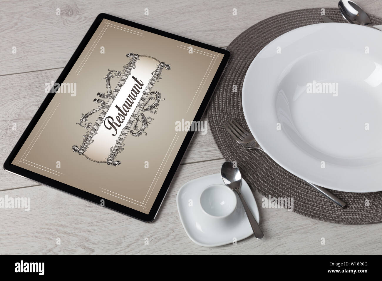 Tablet with stylish restaurant logo and laid table  Stock Photo