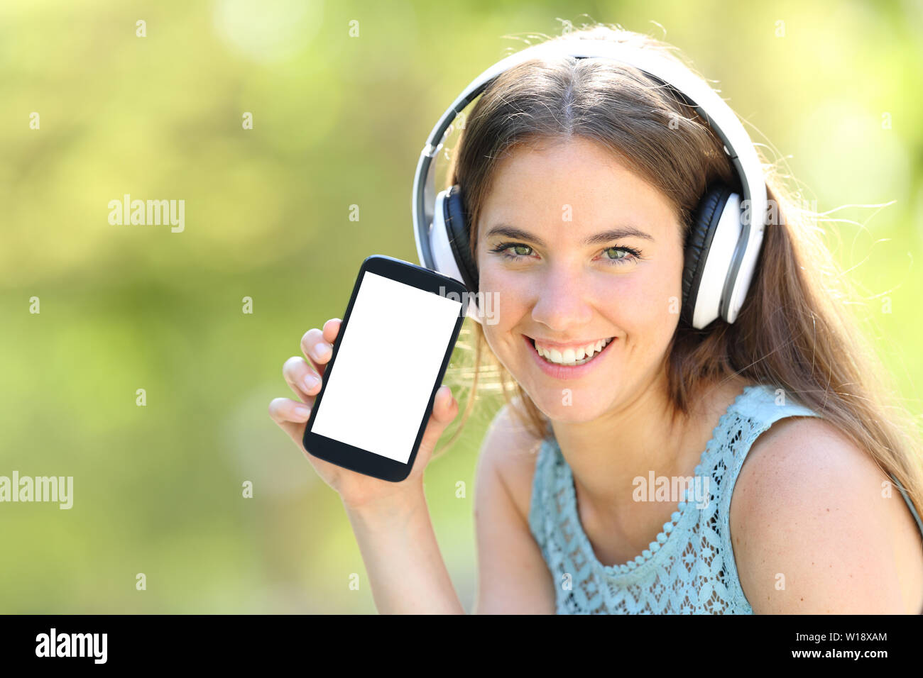 Girl with headphones showing blank smart phone screen in a park with a