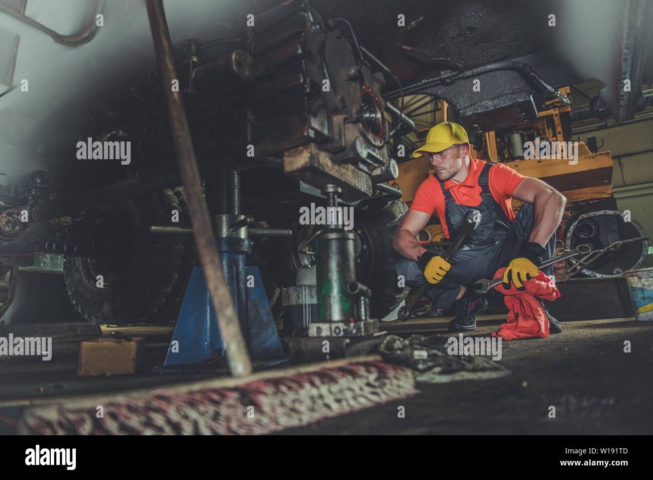 Heavy Equipment Repair Shop. Caucasian Professional Mechanic Fixing Excavator Undercarriage