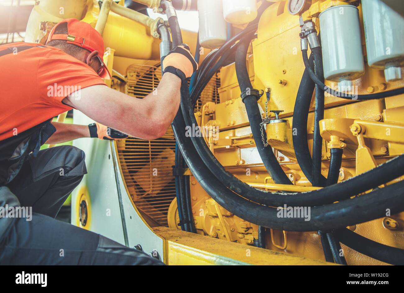 Caucasian Professional Mechanic Fixing Bulldozer Engine Inside Heavy Equipment Repair Shop. Stock Photo