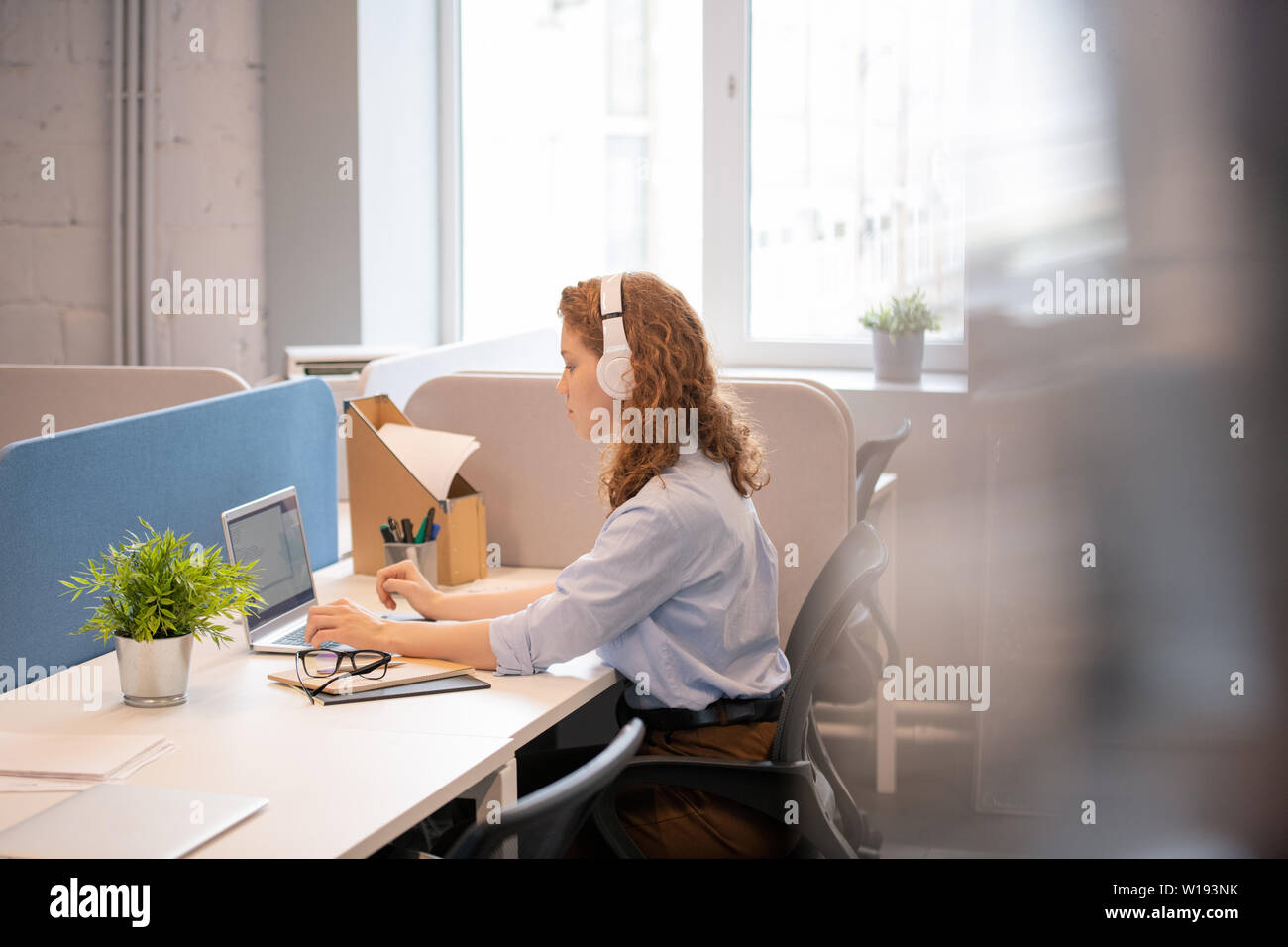 Serious focused young woman with red hair wearing headphones sitting at ...