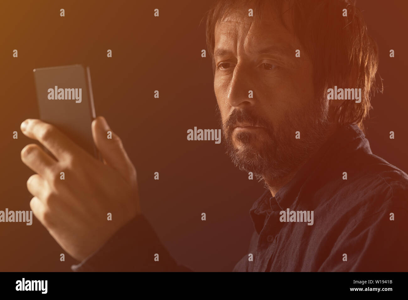 Adult man looking at mobile phone screen. Portrait of caucasian male with beard using modern smartphone. Stock Photo