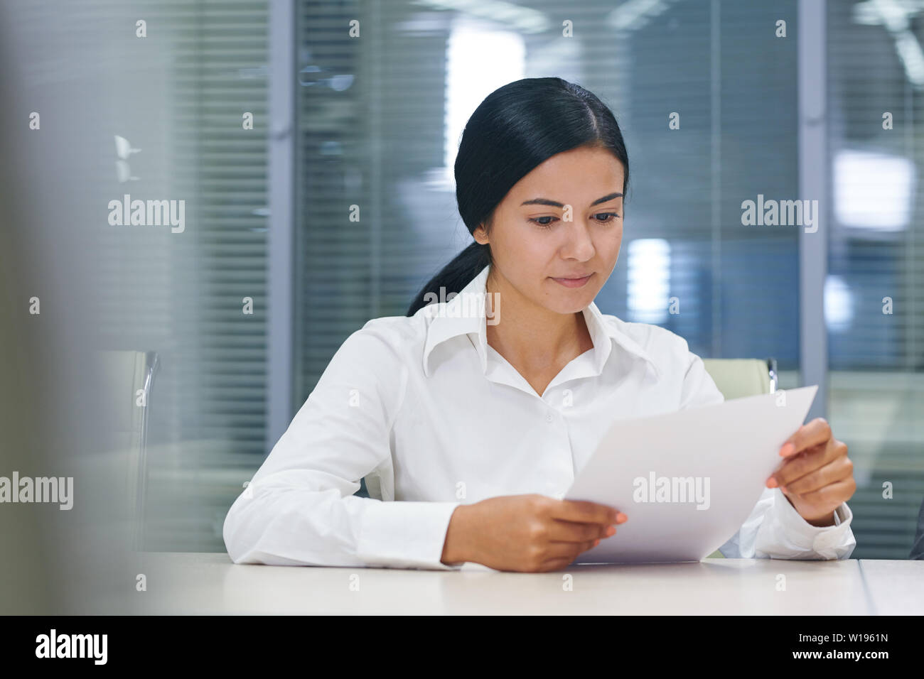 Pretty young brunette businesswoman reading financial document in office Stock Photo