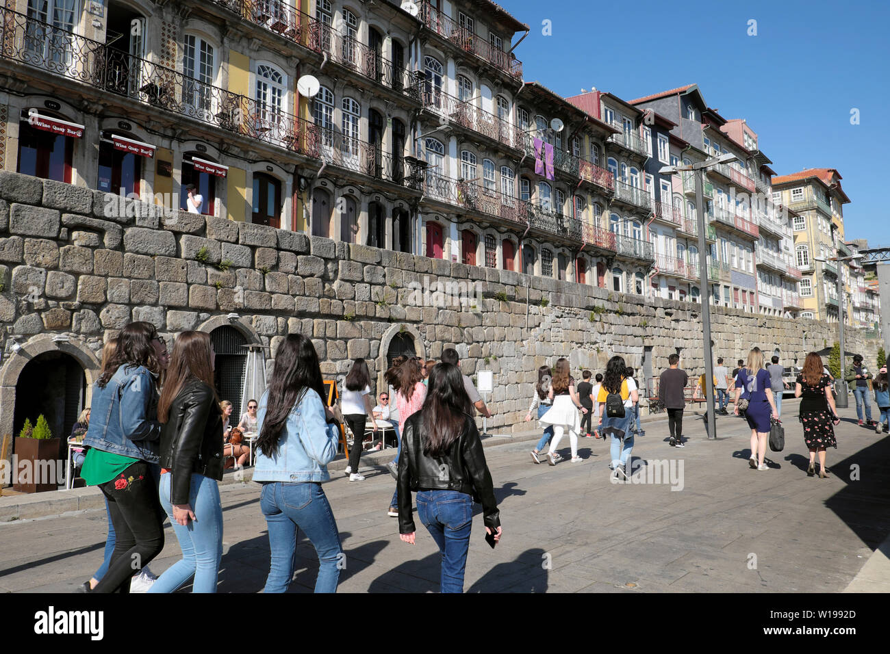 Students young women rear view walking along quay in Ribeira with a view of apartments housing in Porto Oporto Portugal Europe  KATHY DEWITT Stock Photo