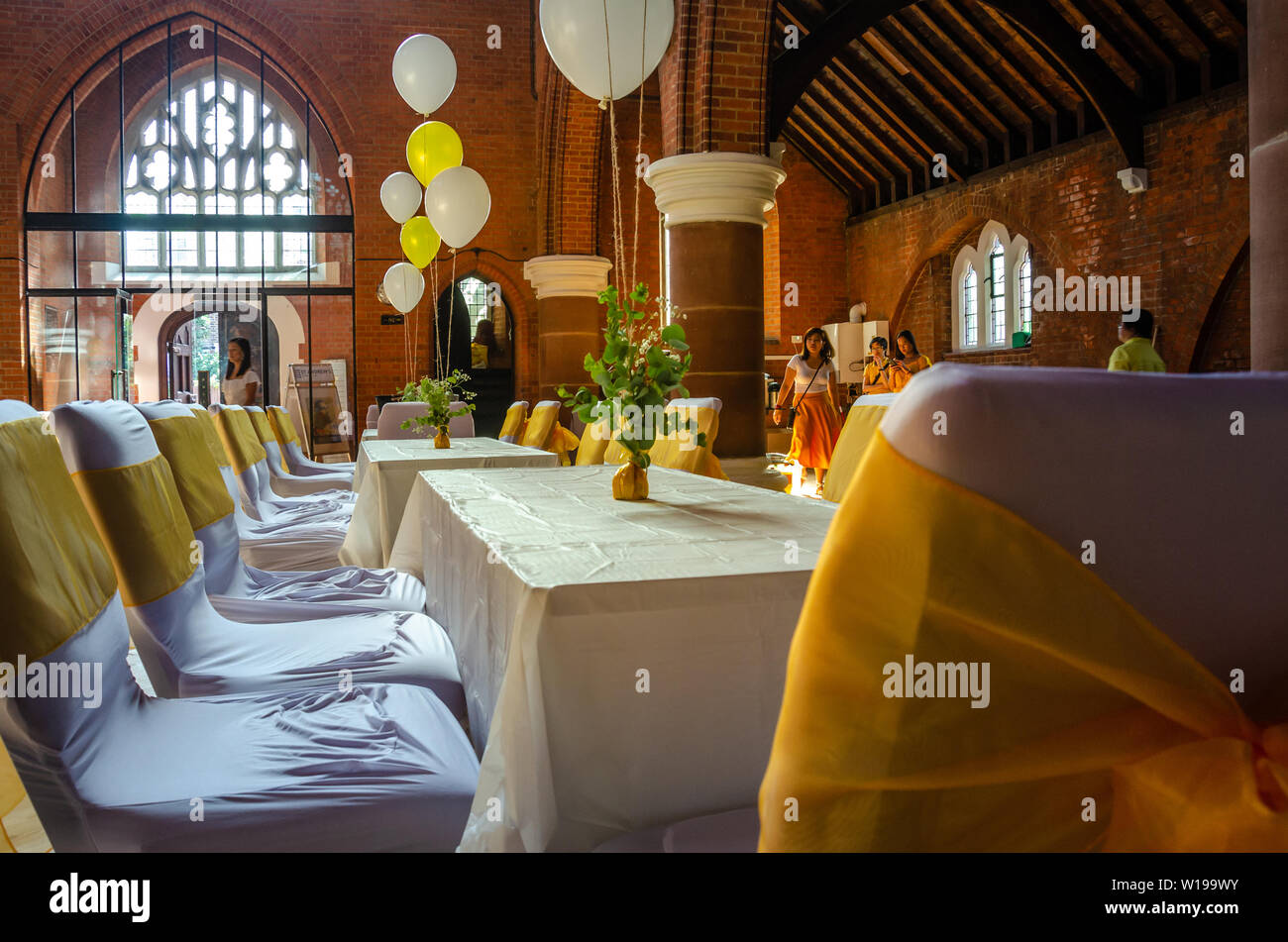 Tables and chairs set out in a church hall, decorated with helium filled balloons and yellow ribbons ready for a party, reception or celebration Stock Photo