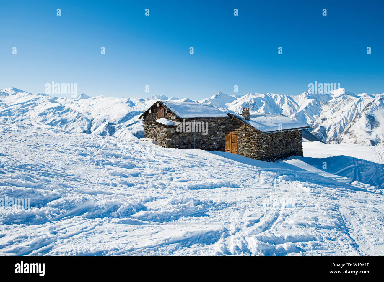 Panoramic view of snow covered mountains in an alpine ski resort with stone building on remote slope Stock Photo