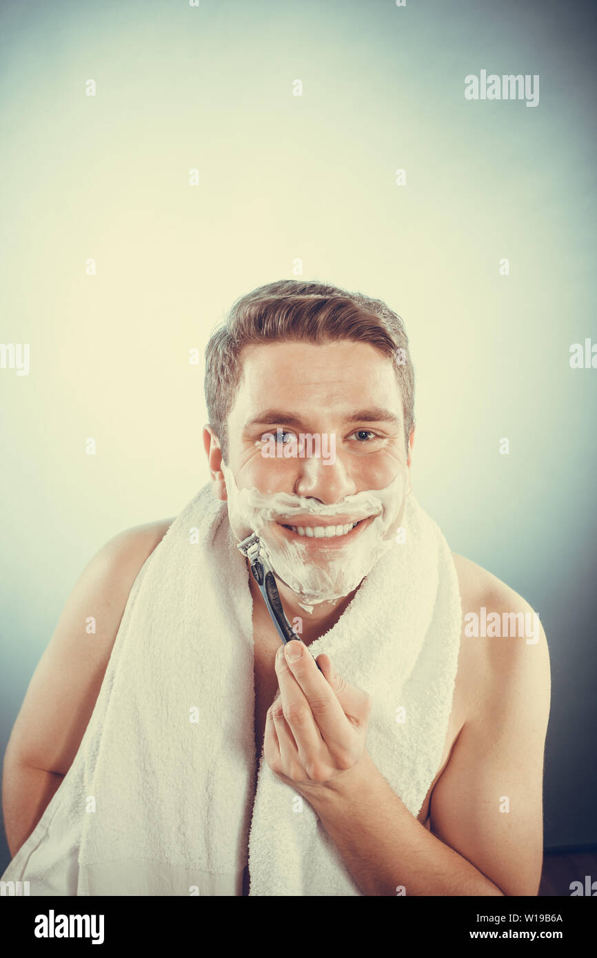 Happy smiling man shaving using razor with cream foam. Handsome guy