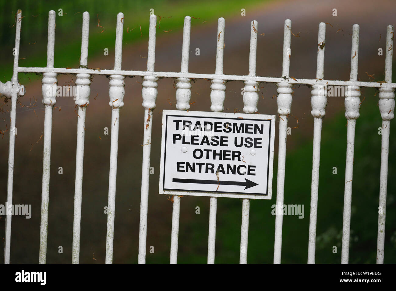 'Tradesmen please use other entrance' sign on a white iron fence. Stock Photo