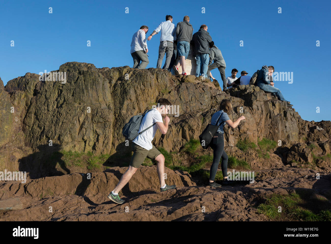 In summer evening sunshine, walkers climb the last metres to the summit of Arthur's Seat in Holyrood Park that overlooks the city of Edinburgh, on 26th June 2019, in Edinburgh, Scotland. Arthur's Seat is an extinct volcano which is considered the main peak of the group of hills in Edinburgh, Scotland, which form most of Holyrood Park, described by Robert Louis Stevenson as 'a hill for magnitude, a mountain in virtue of its bold design'. The hill rises above the city to a height of 250.5 m (822 ft), providing excellent panoramic views of the city and beyond. Stock Photo
