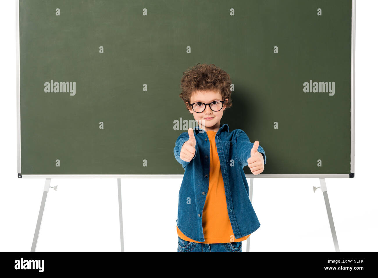 smiling schoolboy in glasses standing near blackboard and showing ...