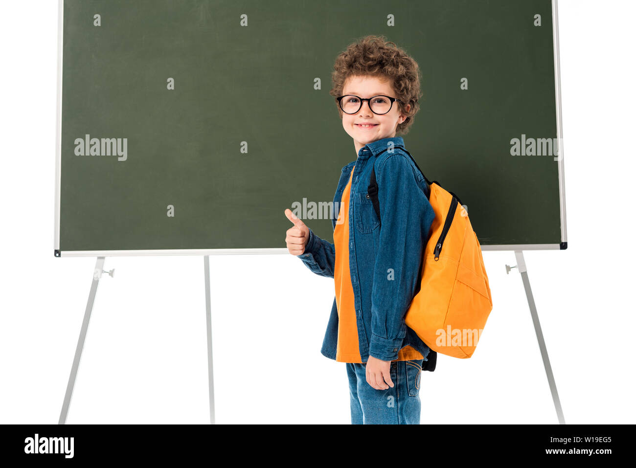 smiling schoolboy in glasses standing near blackboard and showing thumb ...