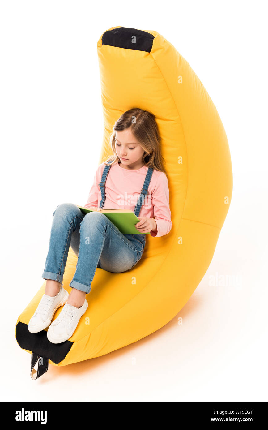 kid in casual clothes sitting on bean bag chair and reading book on