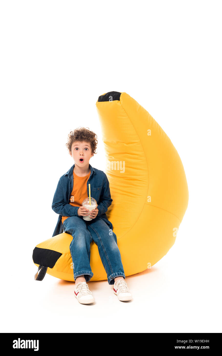 shocked child in jeans sitting on bean bag chair and holding milkshake