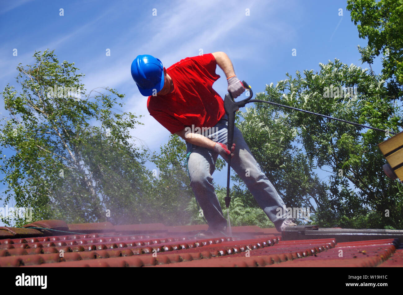 House roof cleaning with pressure tool. Worker on top of building