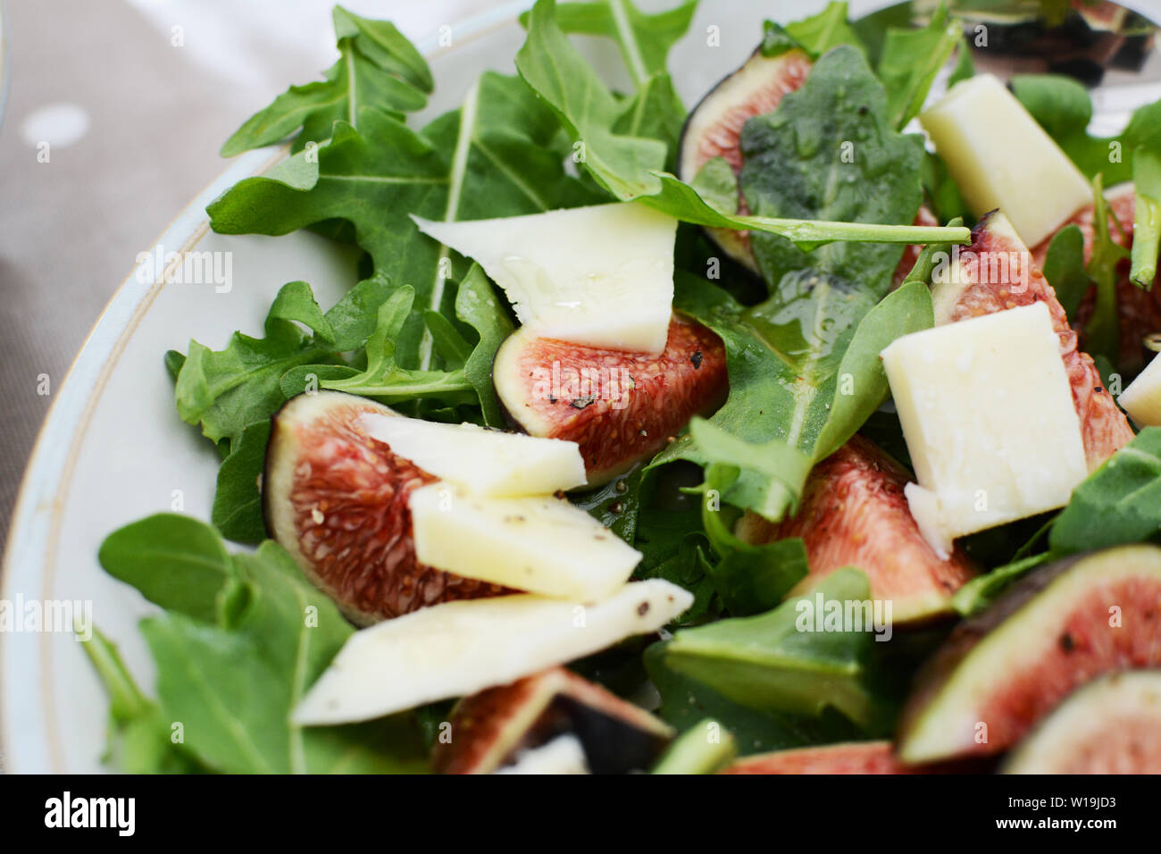 Fresh fig and pecorino chunks on a bed of green rocket leaves, drizzled with honey for a tasty salad Stock Photo