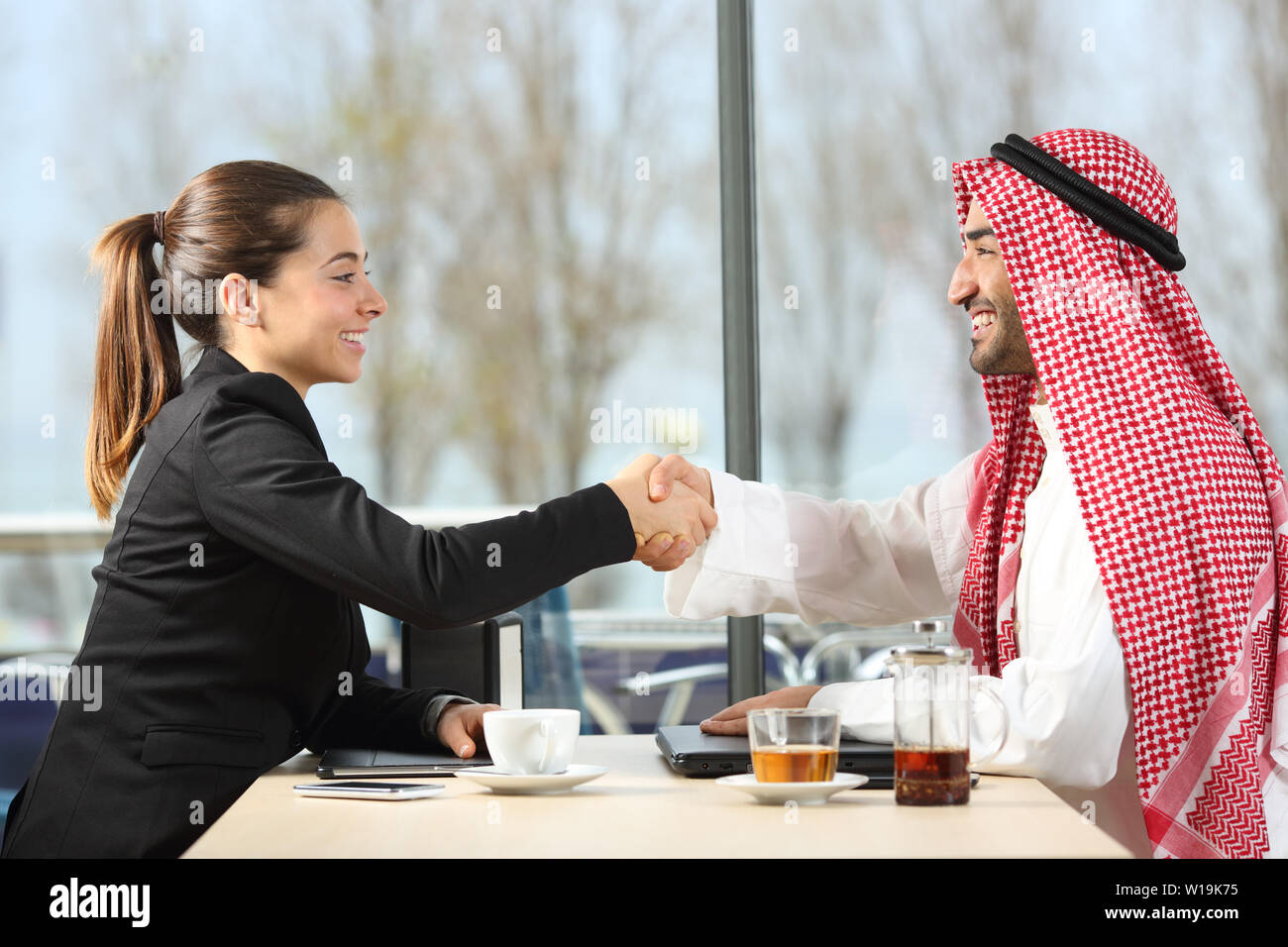 Side view portrait of an arab businessman and businesswoman handshaking in a coffee shop or hotel bar Stock Photo