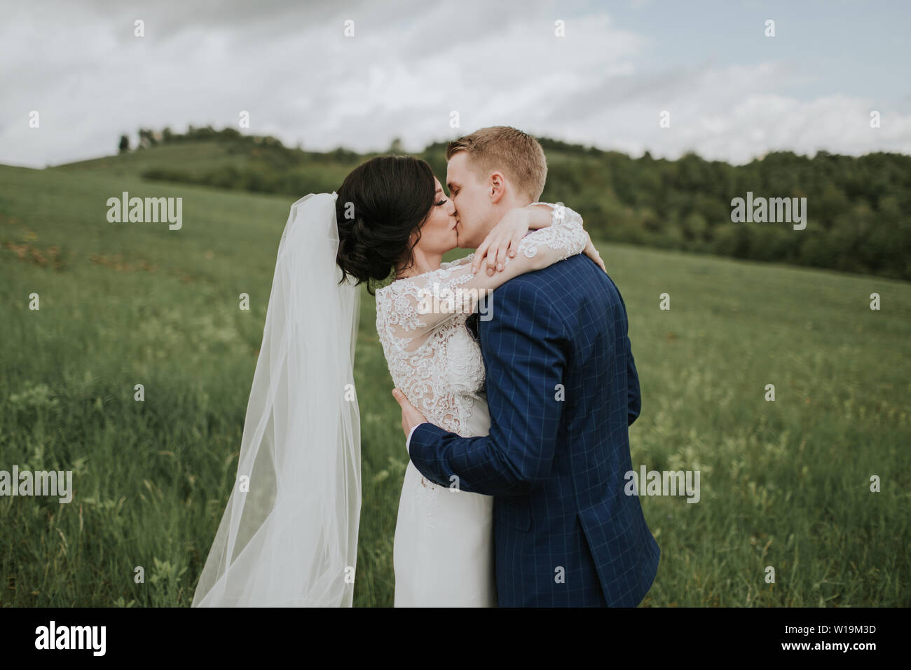 Bride and groom kissing on their wedding day. Just married couple in love hugging outside in nature. Stock Photo