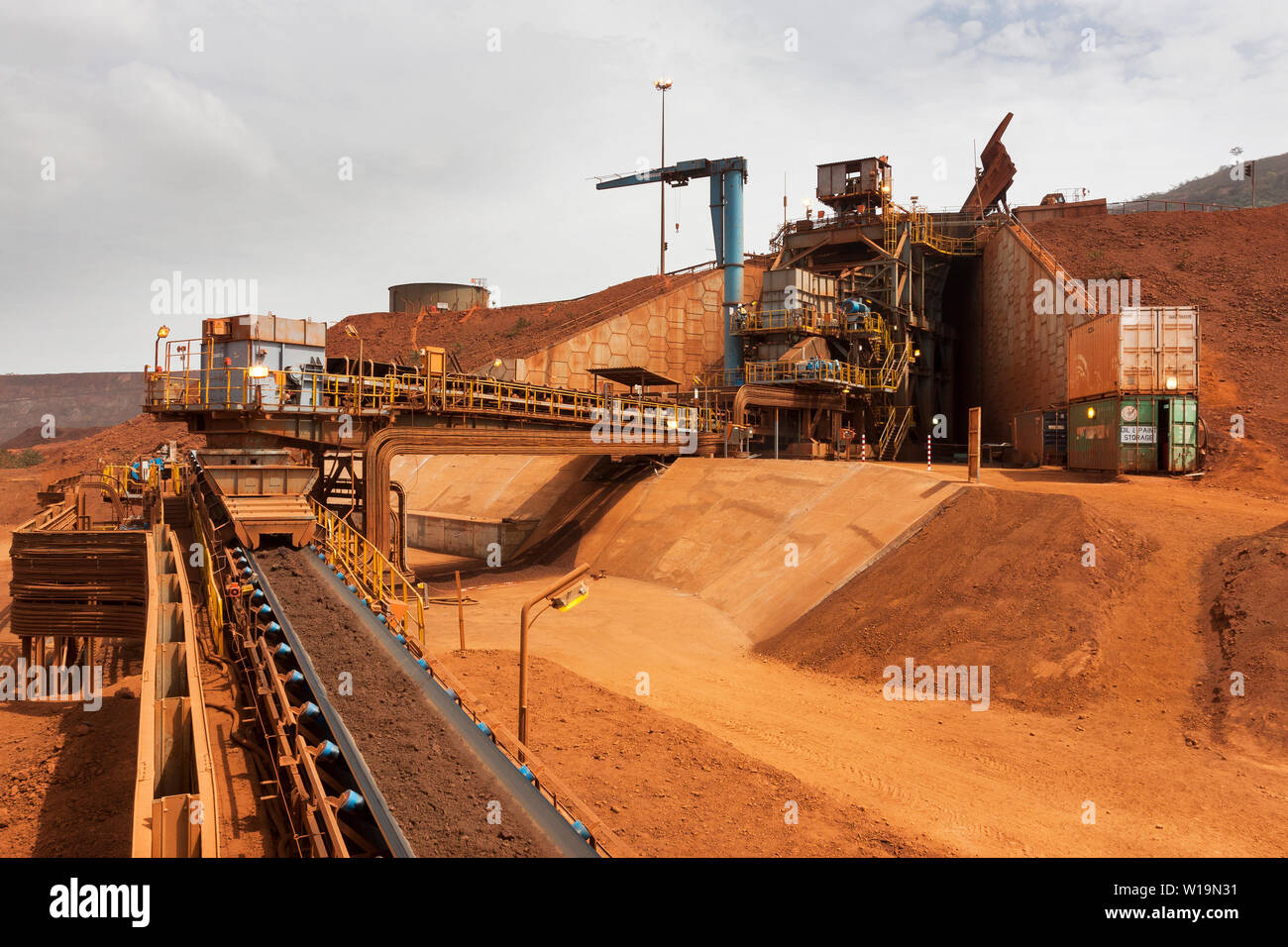 Mining operations for transporting & managing iron ore. Primary crusher with lump ore on conveyor belt and truck unloading product into hopper at top Stock Photo