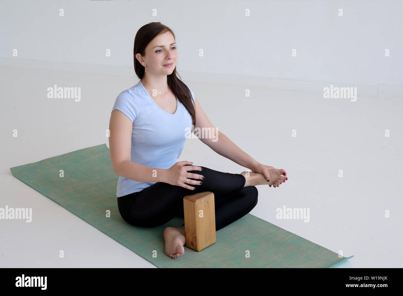 Smiling young woman sitting in Ardha Padmasana with props for hip opening, Stock Photo