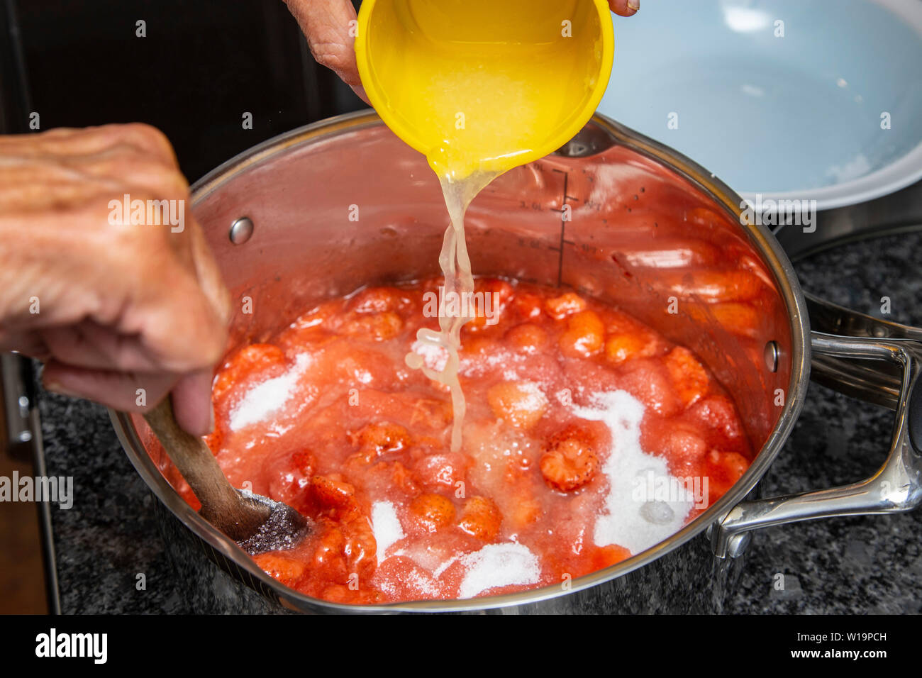 Adding lemon juice to sugar and strawberries as strawberry jam is made on an induction hob in a stainless steel pan. Stock Photo