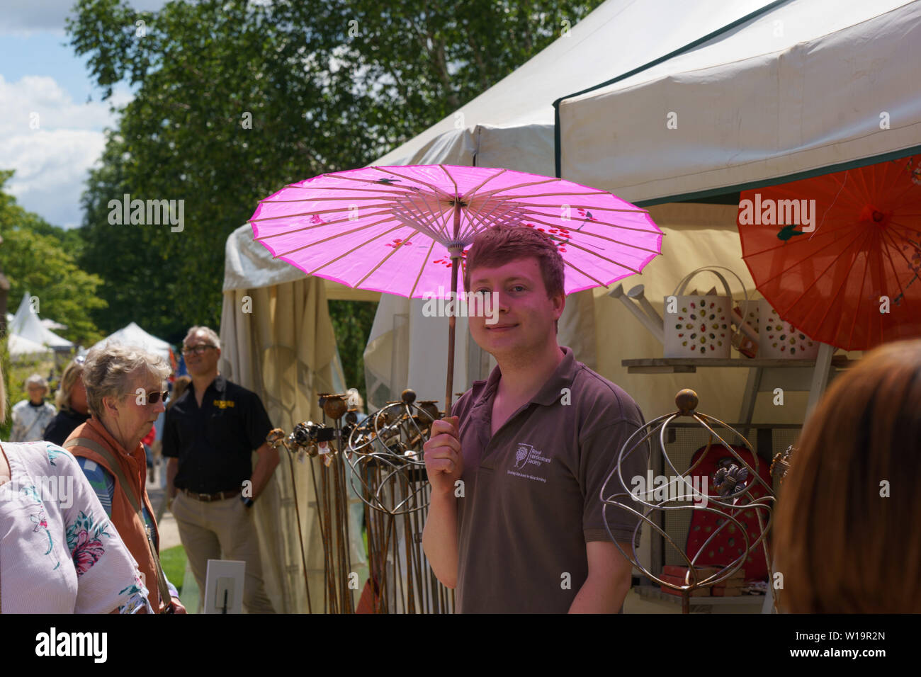 Guy stood by a trade tent and taking shade under a pink Umbrella at a flower show, Harrogate, North Yorkshire, England, UK. Stock Photo