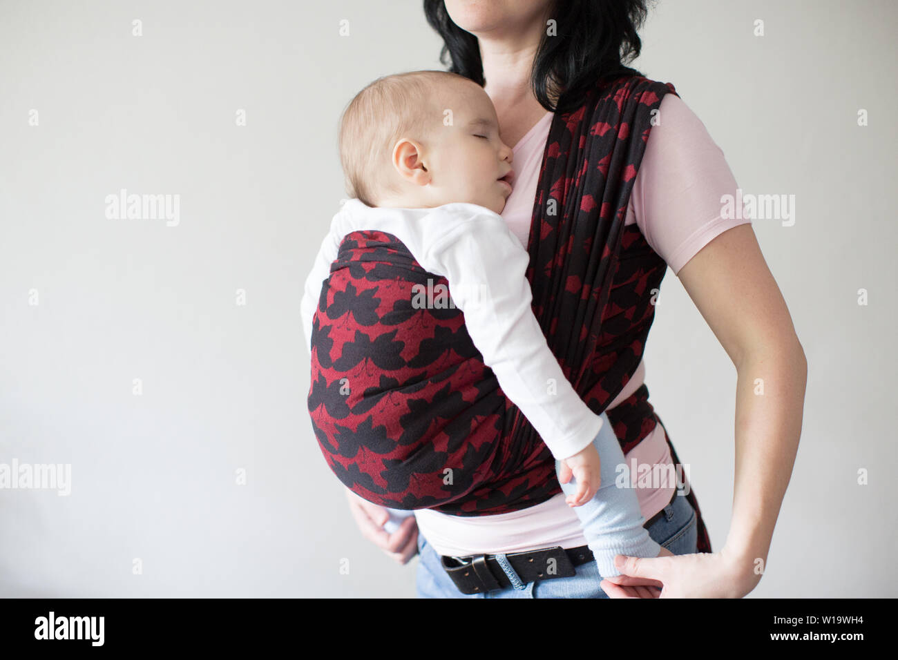 A cropped view of a baby in a woven wrap. A babywearing mother carrying