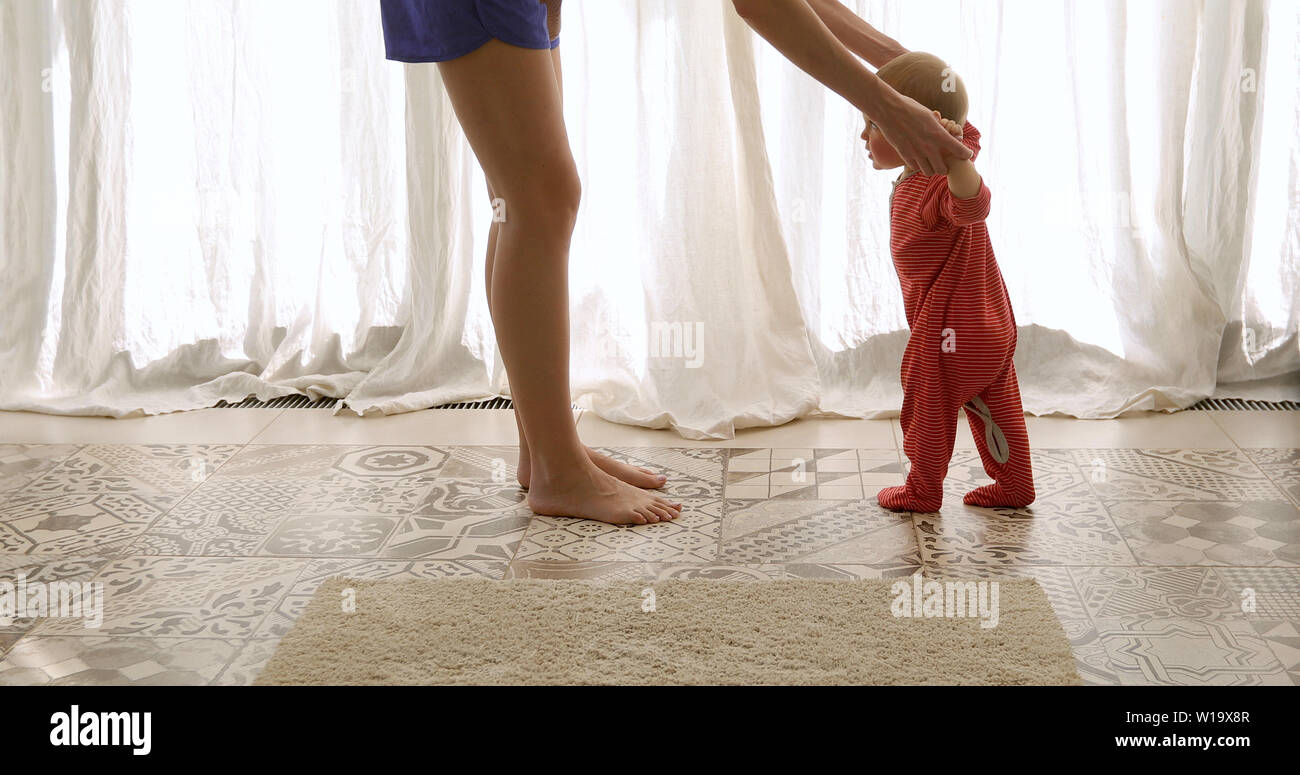 Baby taking first steps with mother help Stock Photo
