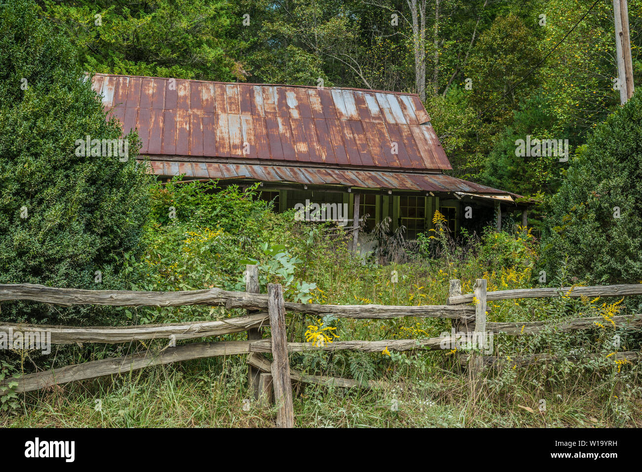 Old abandoned farmhouse in the mountains with a rustic handmade fence and tall weeds surrounding the land Stock Photo