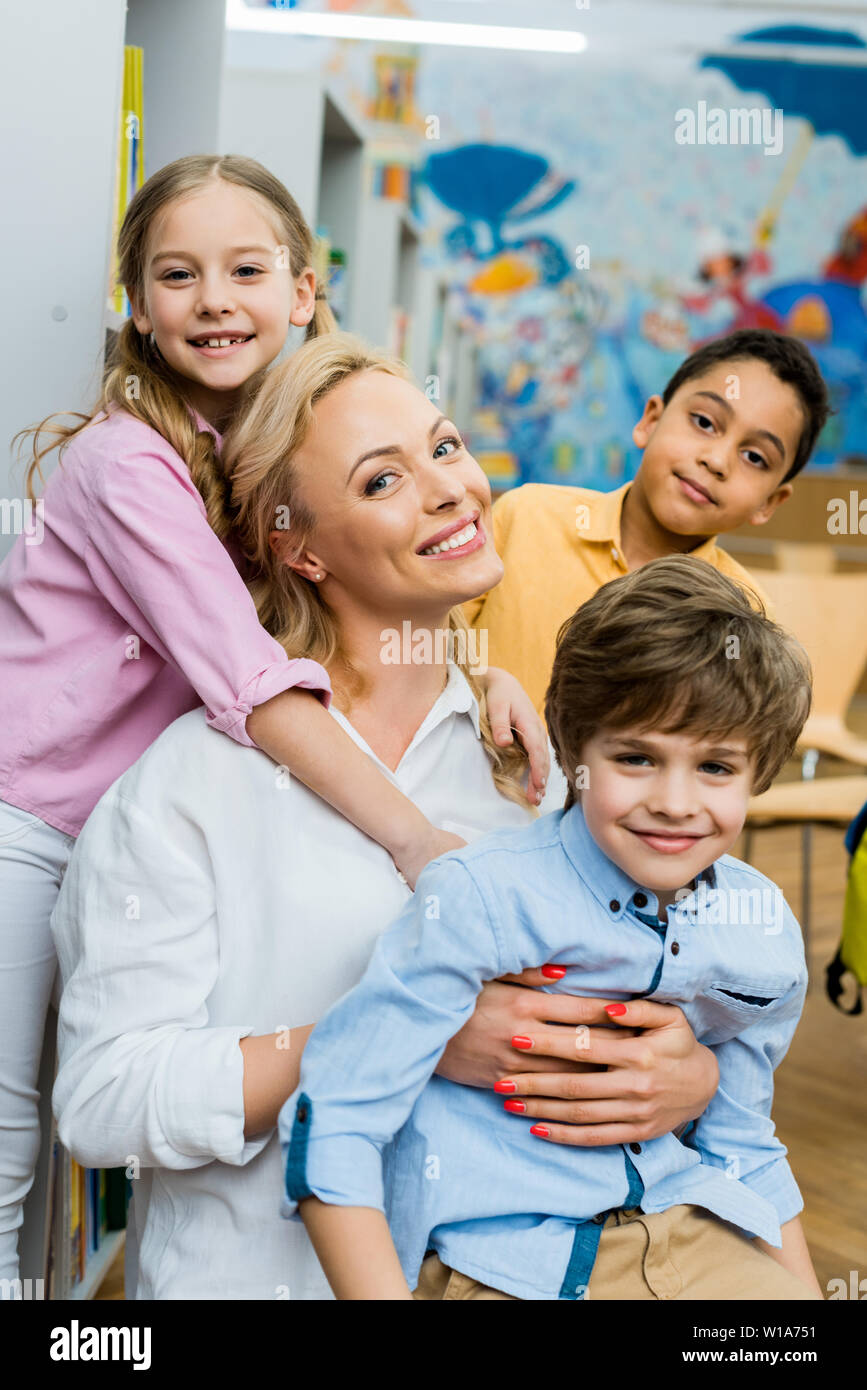 cheerful kid hugging attractive woman near multicultural boys Stock Photo