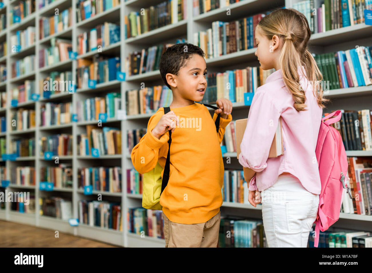 cute multicultural kids standing and talking in library Stock Photo
