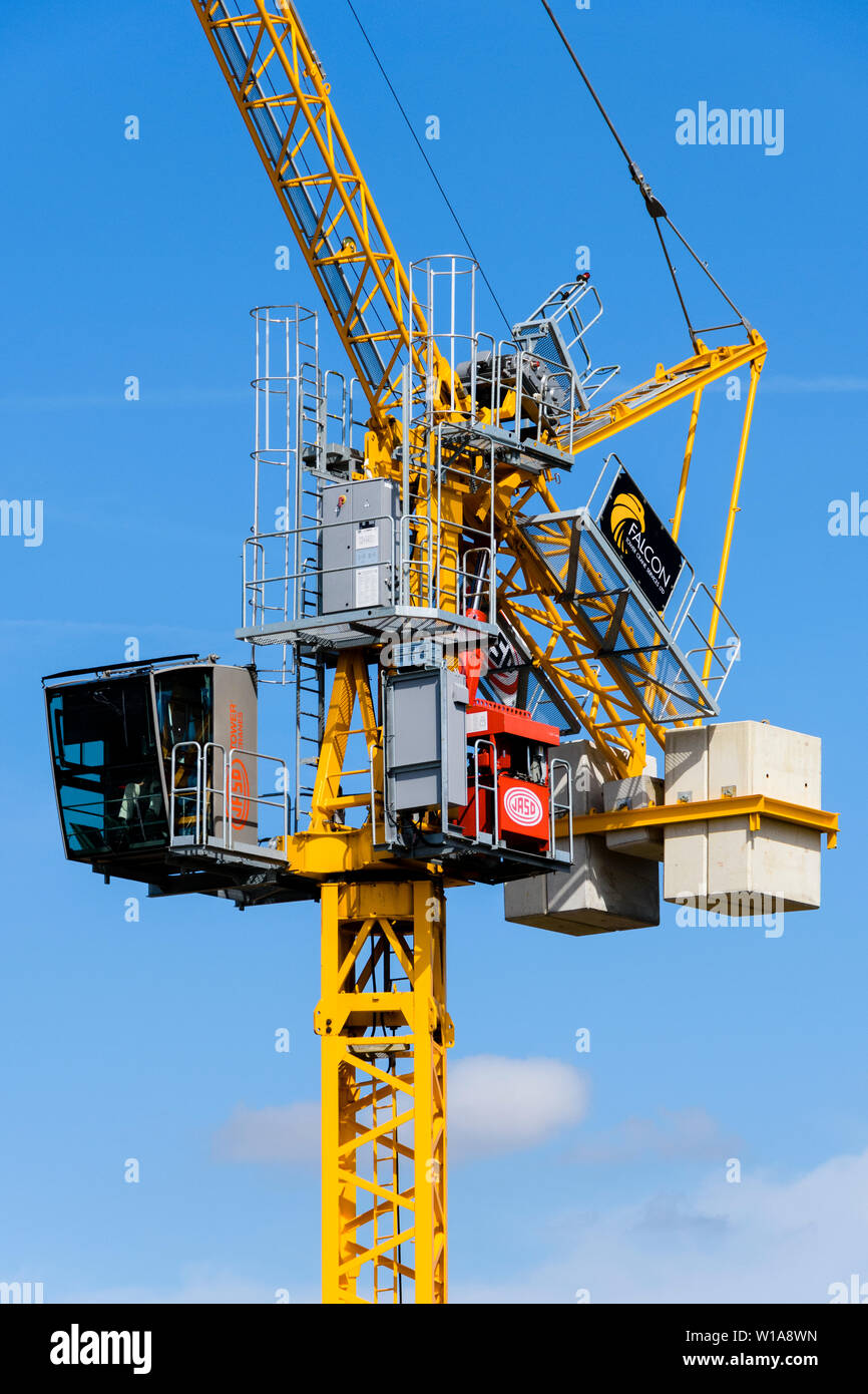 Tall yellow tower crane lifting & working on construction site against