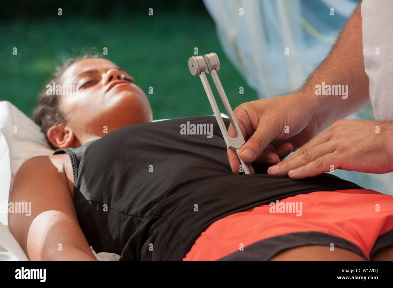 A young woman lying on the couch undergoes chakra stimulation with a tuning fork Stock Photo