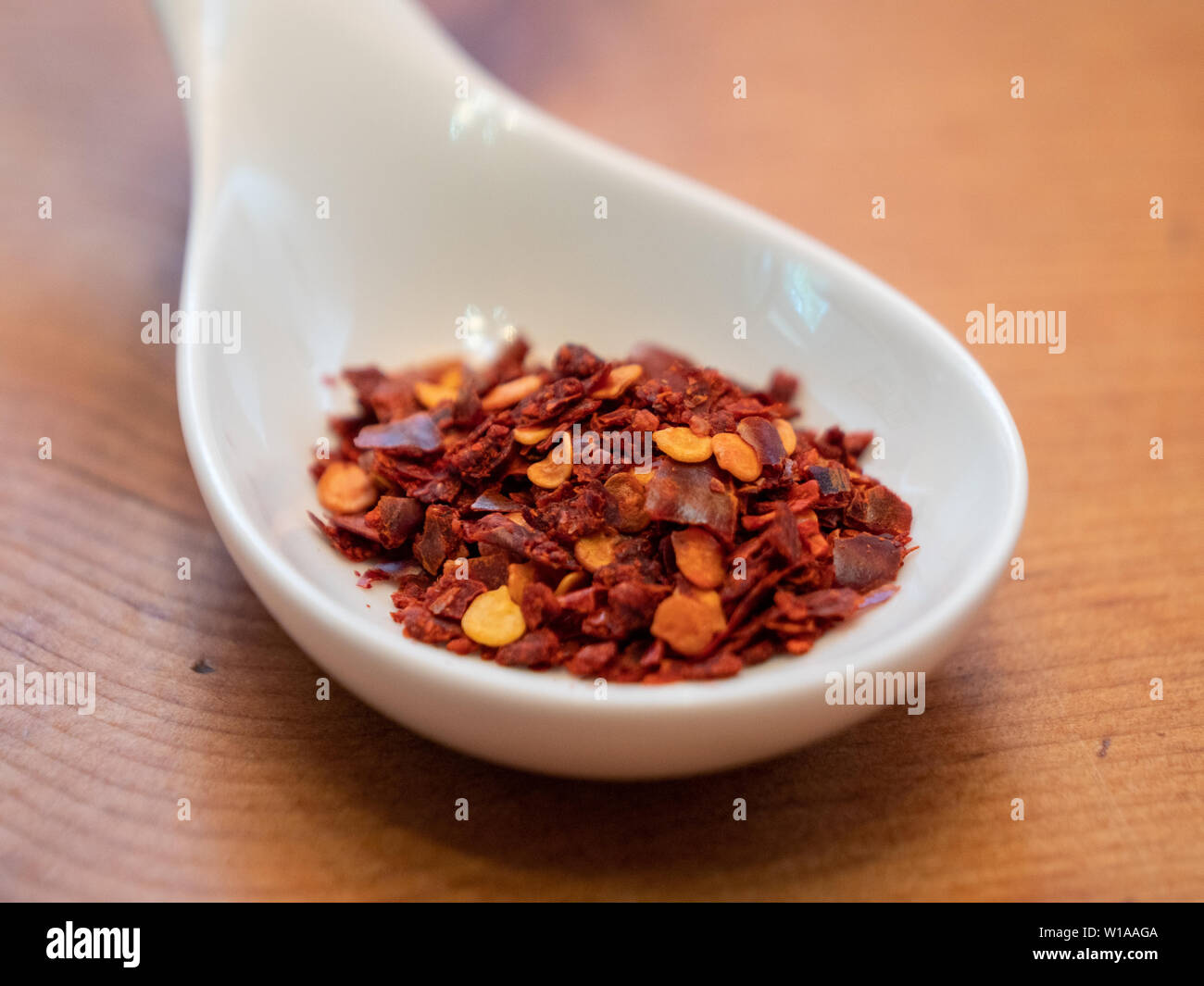 Turkish Red Pepper Flakes in a White Porcelain Spoon on a Wood Table Stock Photo