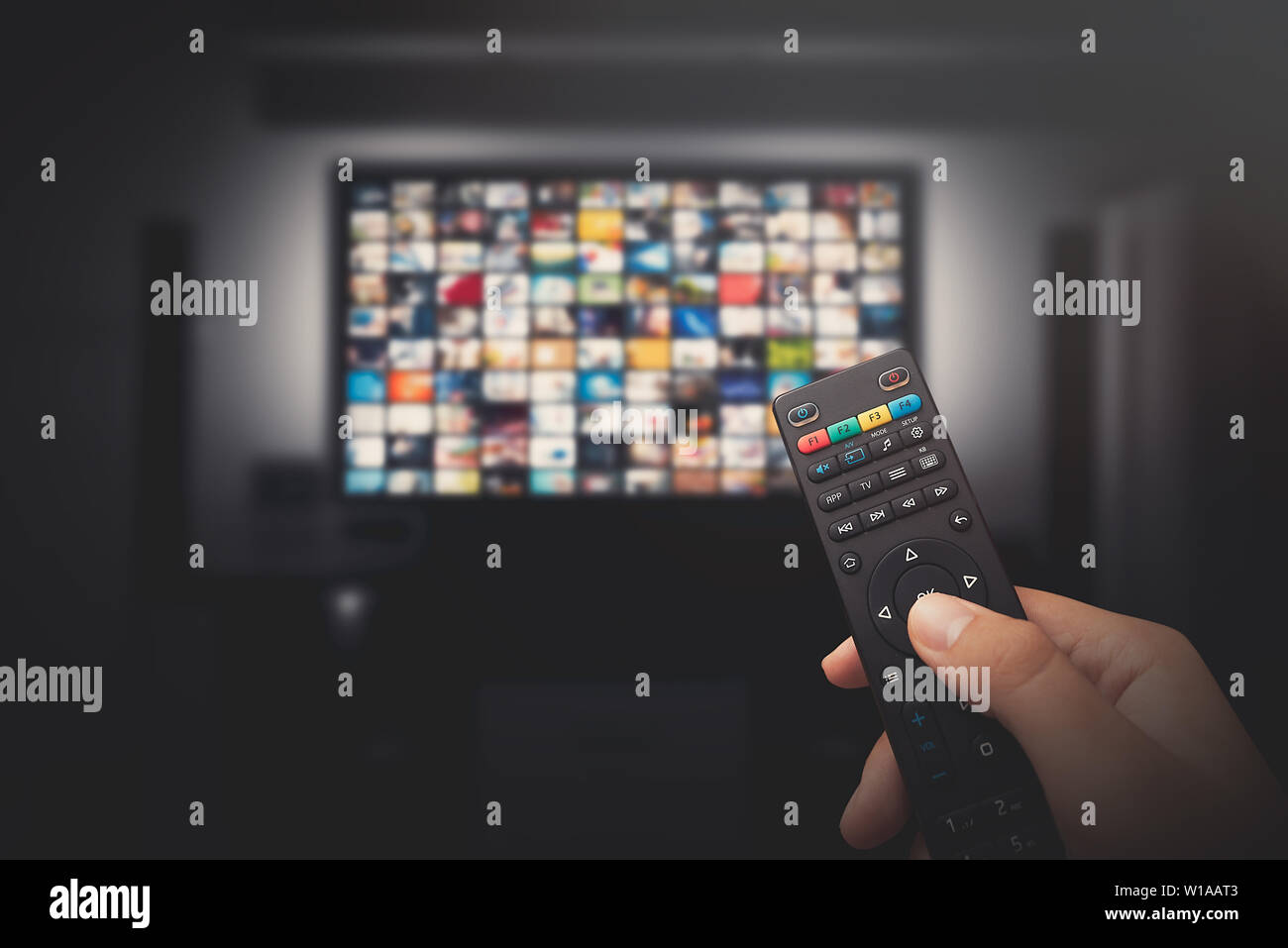 Multimedia video concept on TV set in dark room. Man watching TV with remote control in hand. Stock Photo
