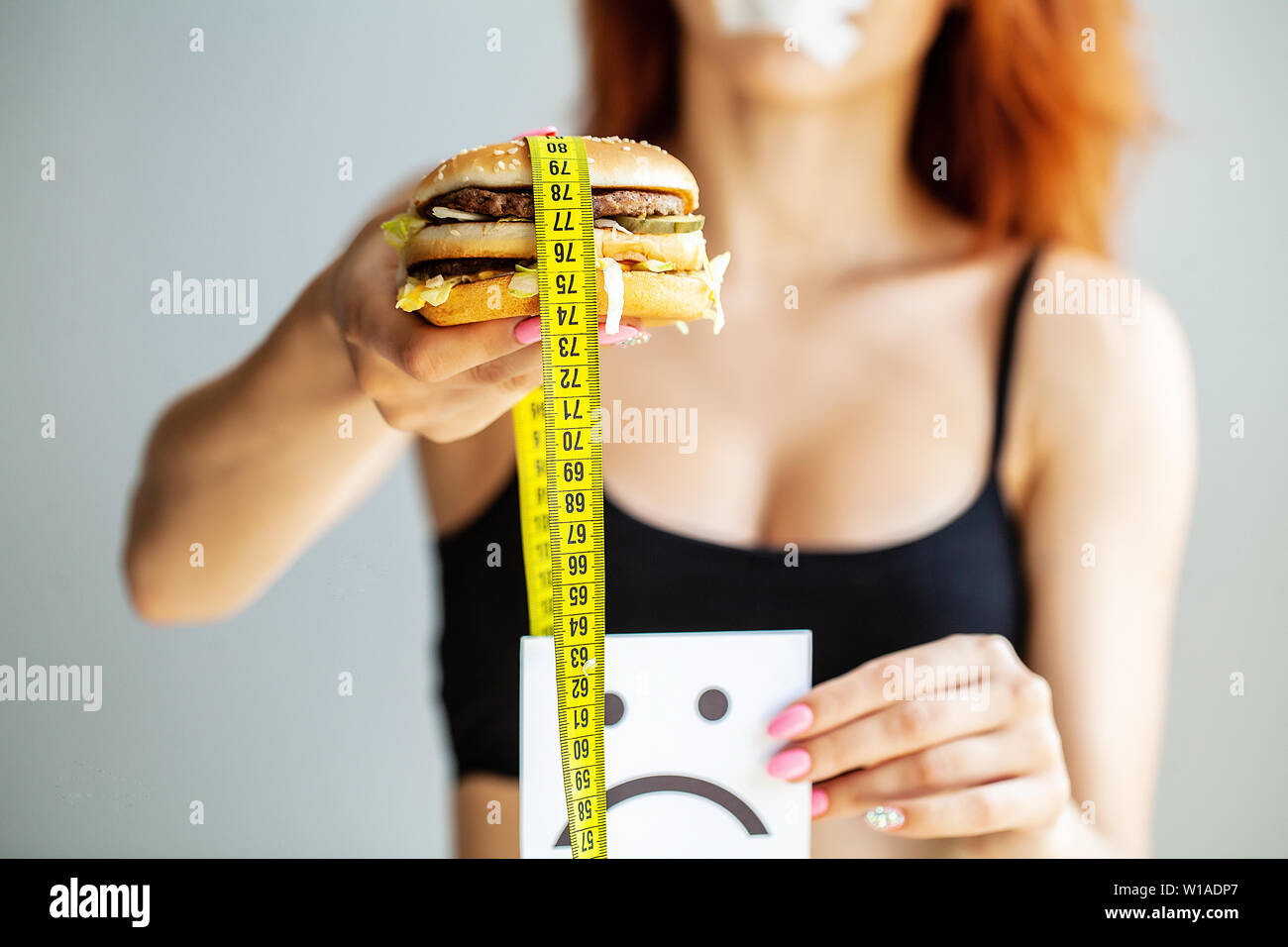 Diet. Portrait woman wants to eat a Burger but stuck skochem mouth, the concept of diet, junk food, willpower in nutrition. Stock Photo
